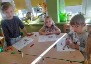 Grupa dzieci wykonuje pracę plastyczną przy stoliku.